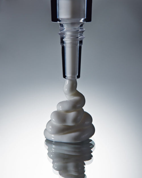 Carica immagine 1 in visualizzazione galleria. White cream being squeezed from a clear container with a black cap onto a reflective surface.
