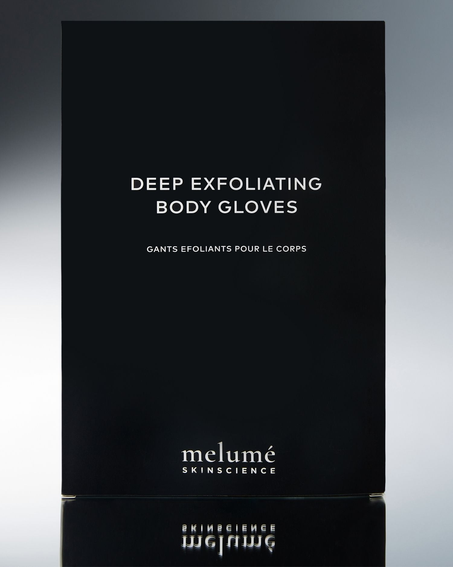 Melumé Skincare Deep Exfoliating Body Gloves packaging box in matte black with white text, shown against a dark gray gradient background with a reflection below.