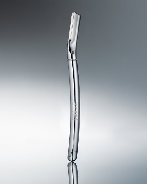 Bild 1 in Galerieansicht laden. A polished stainless steel electric razor standing vertically on a reflective gray surface against a gradient gray background.